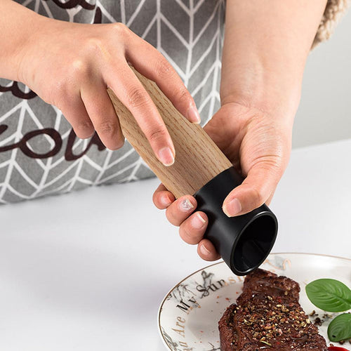 Black adjustable wooden pepper grinder seasoning food at the table