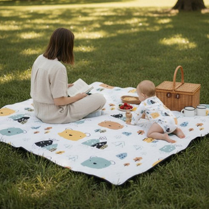 Women and baby sitting outside on a blanket with a wicker basket next to them.